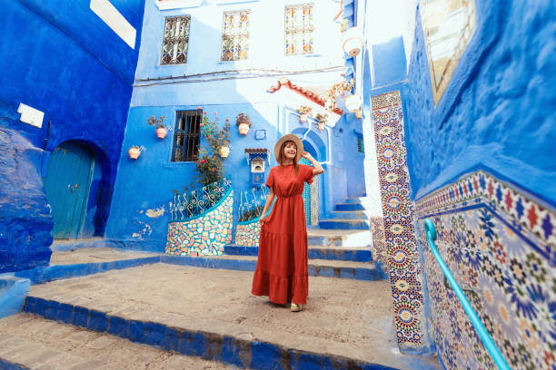 Young woman with red dress visiting the blue city Chefchaouen, Marocco - Happy tourist walking in Moroccan city street - Travel and vacation lifestyle concept